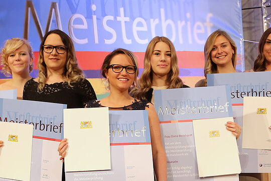 Friseur-Meisterinnen Sieben Meisterinnen im festlichen Outfit mit Meisterbriefen in der Hand, die sich über ihren Abschluss feiern.